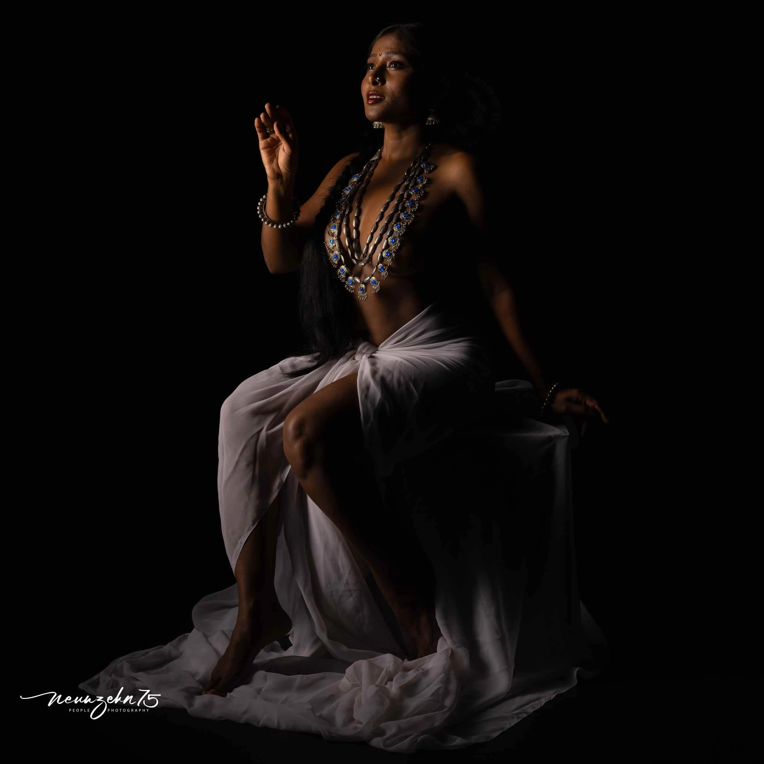 Desi dusky model sitting topless wearing large blue necklace hiding her big tits with it while wearing a white saree in her hips
