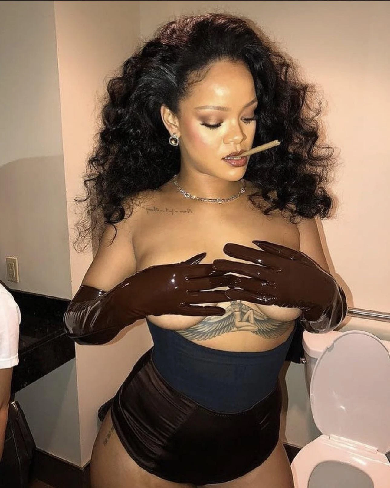 Enchanting celebrity covering her naked boobs while posing topless wearing a black corset and smoking a cigar