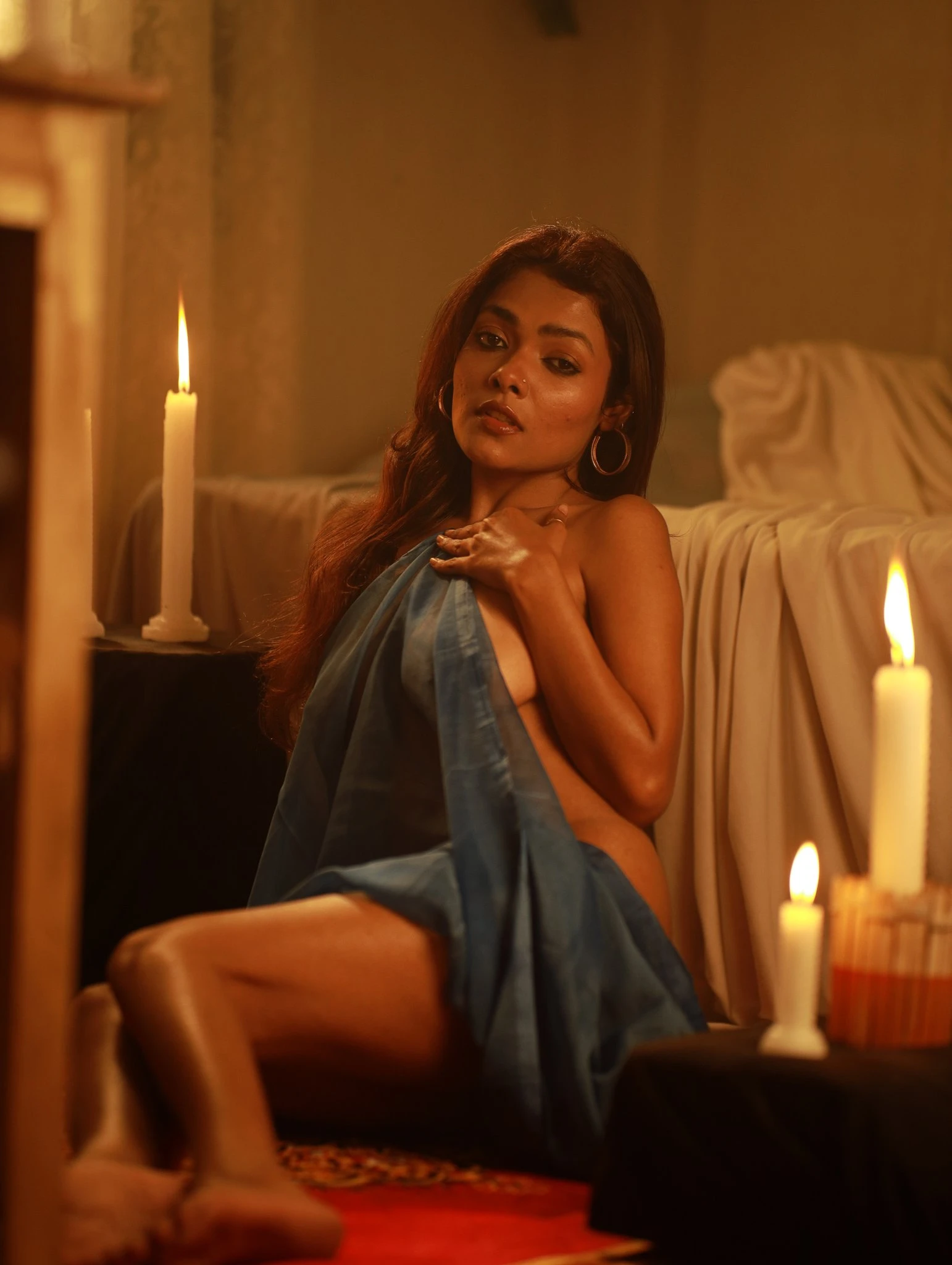 Desi model sitting near bed and candles and showing glimpses of her naked tits and naked body while covering herself with a blue saree