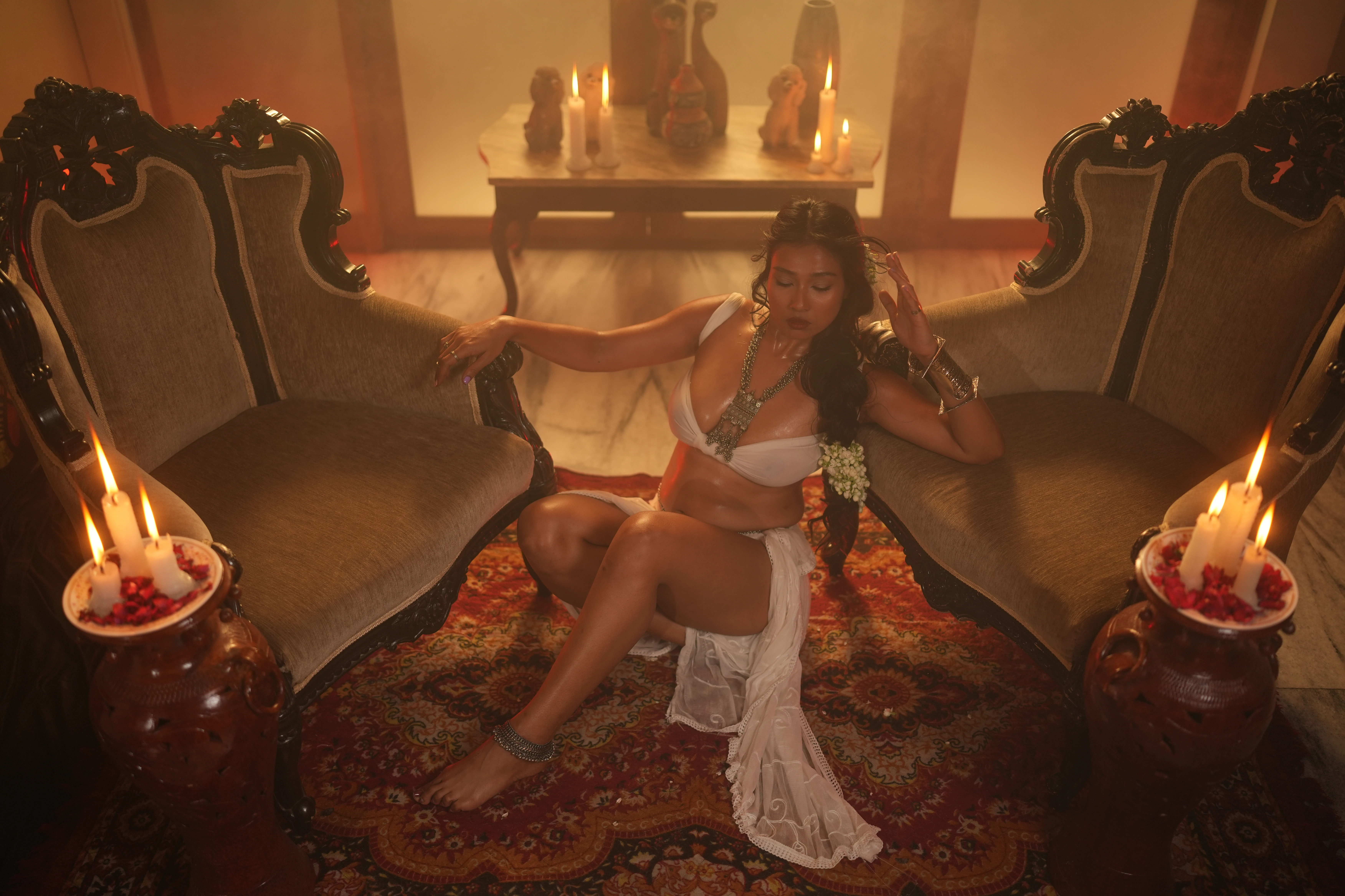 Sultry Desi MILF model showcases her big boobs in a thin breast cloth and shows her nipples while posing near high back chairs and candles