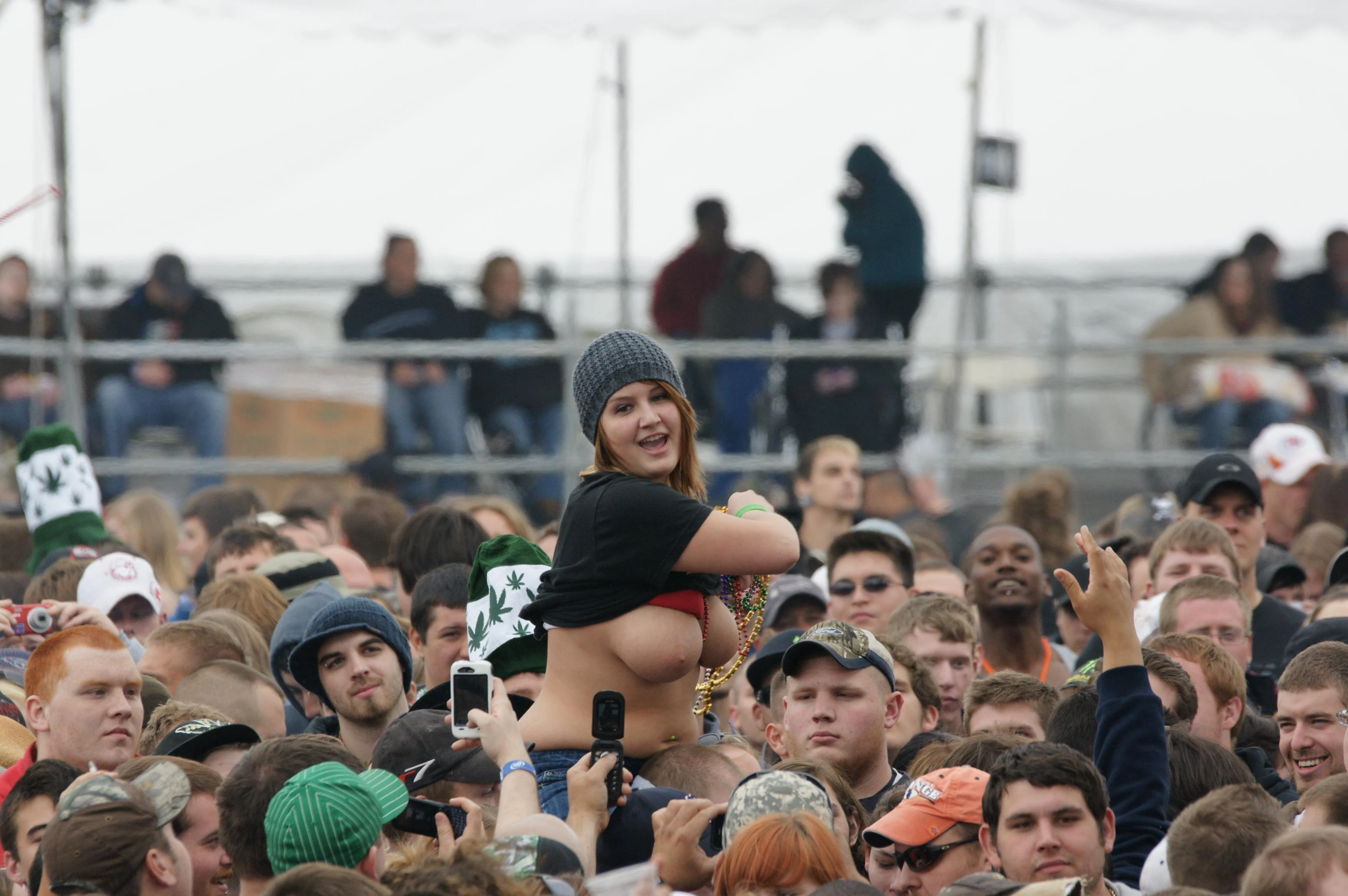 Hot lady wearing beanie cap bares her big boobs while sitting on the shoulder of her friend in a concert