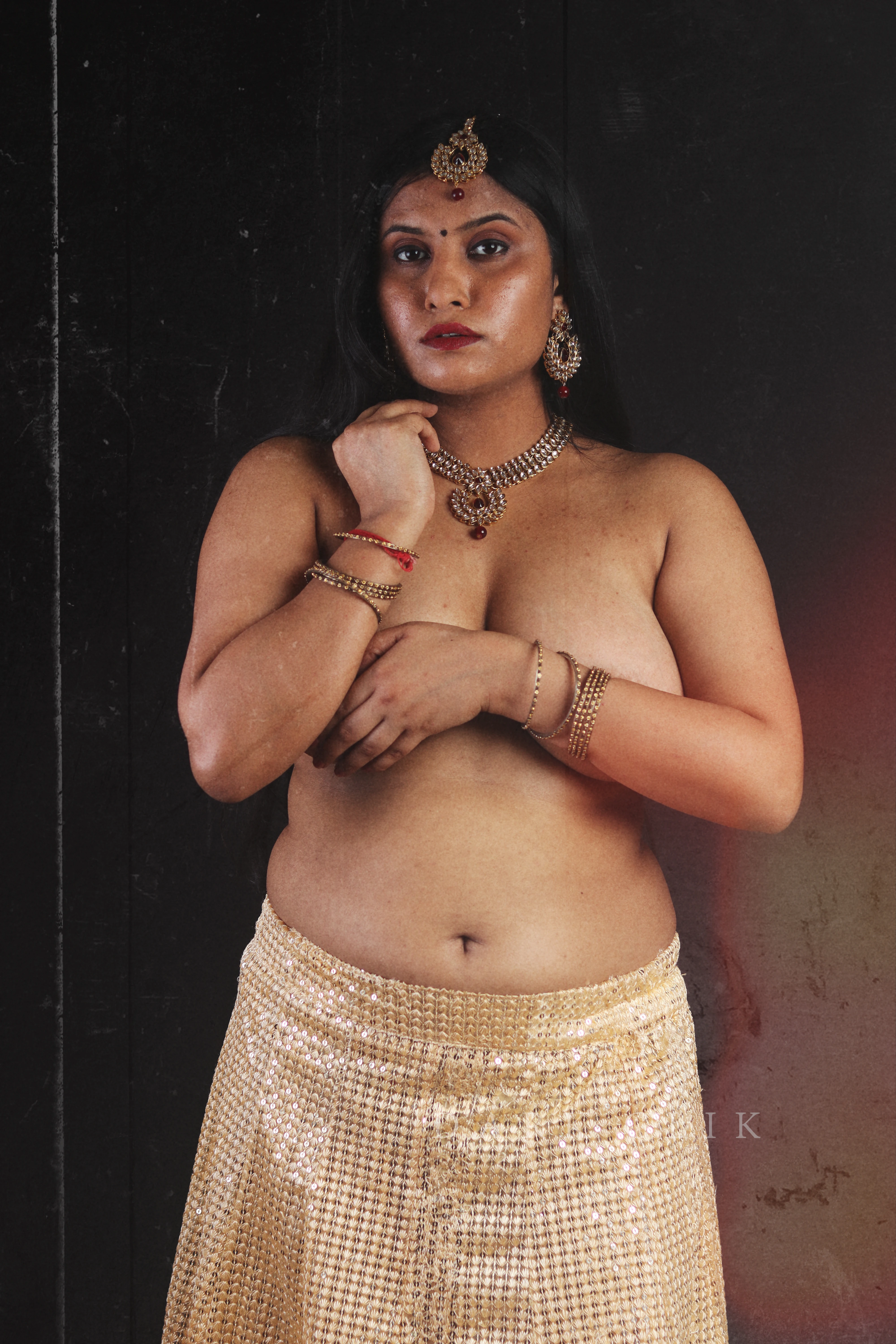 Desi MILF lady wearing jewels poses topless in a golden skirt and hides her naked big boobs with her hand