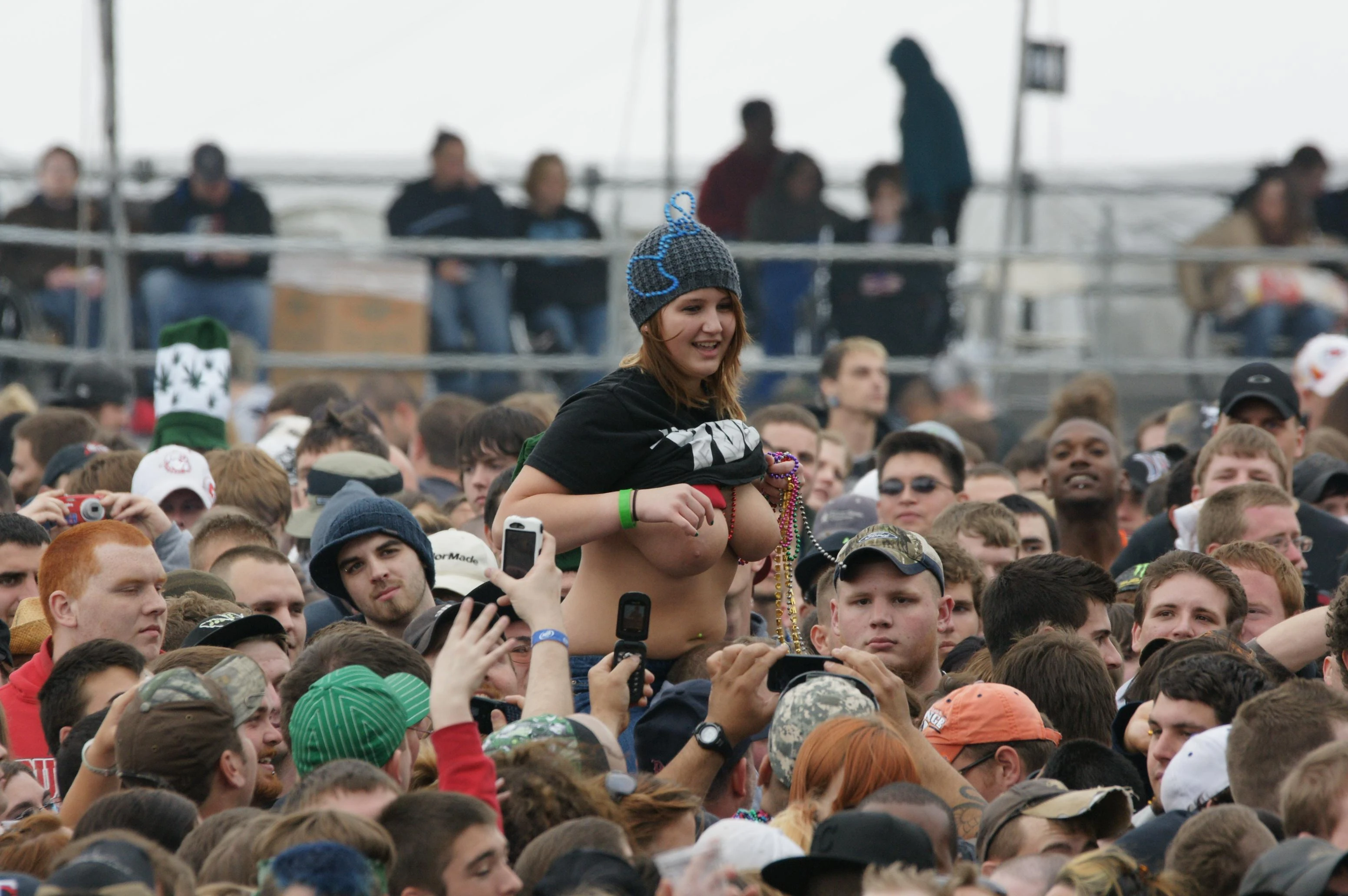 Hot lady wearing beanie cap bares her big tits while sitting on the shoulder of her friend in a concert