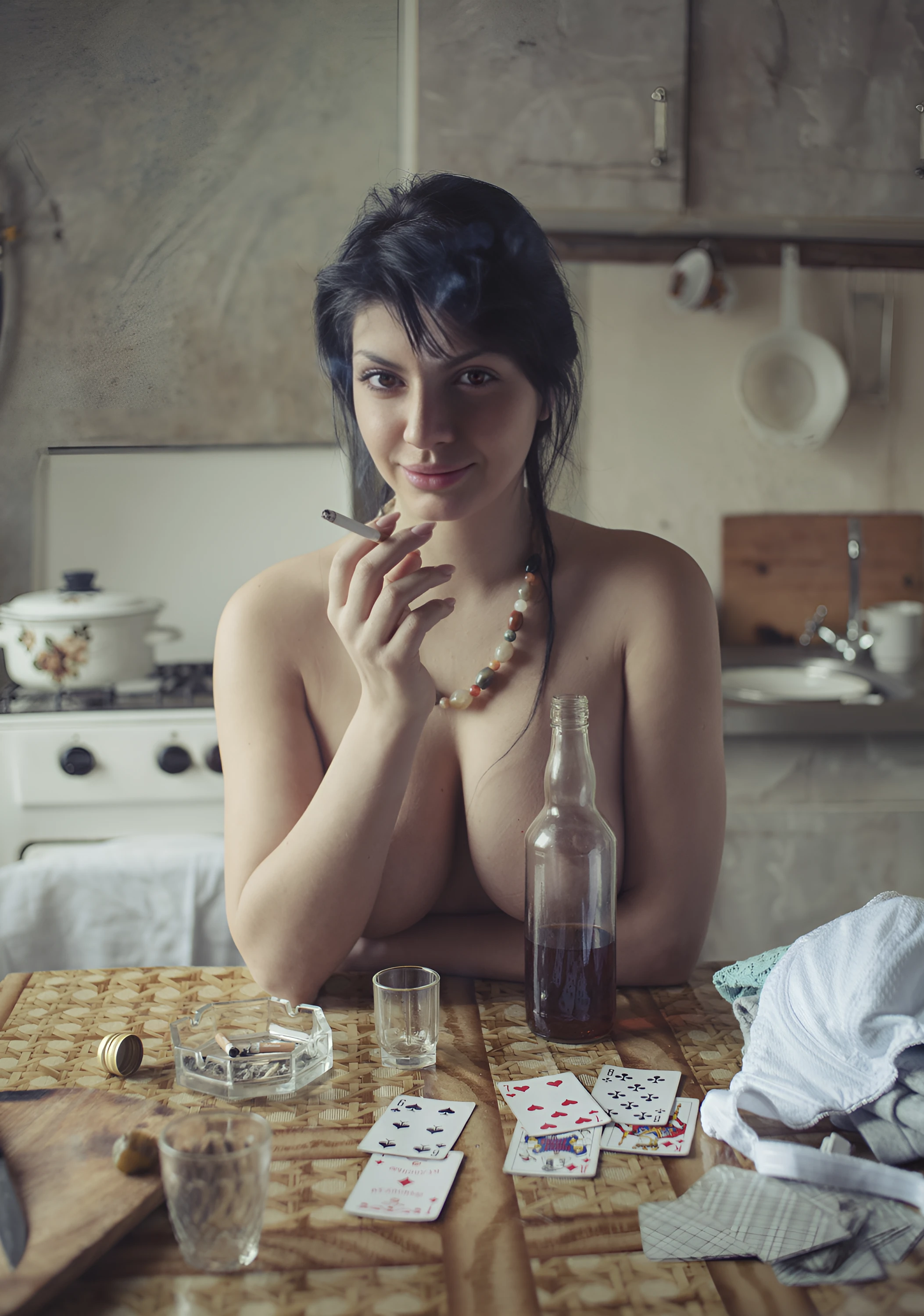 Provocative topless MILF smoking cigarette while sitting on the kitchen but hides her boobs