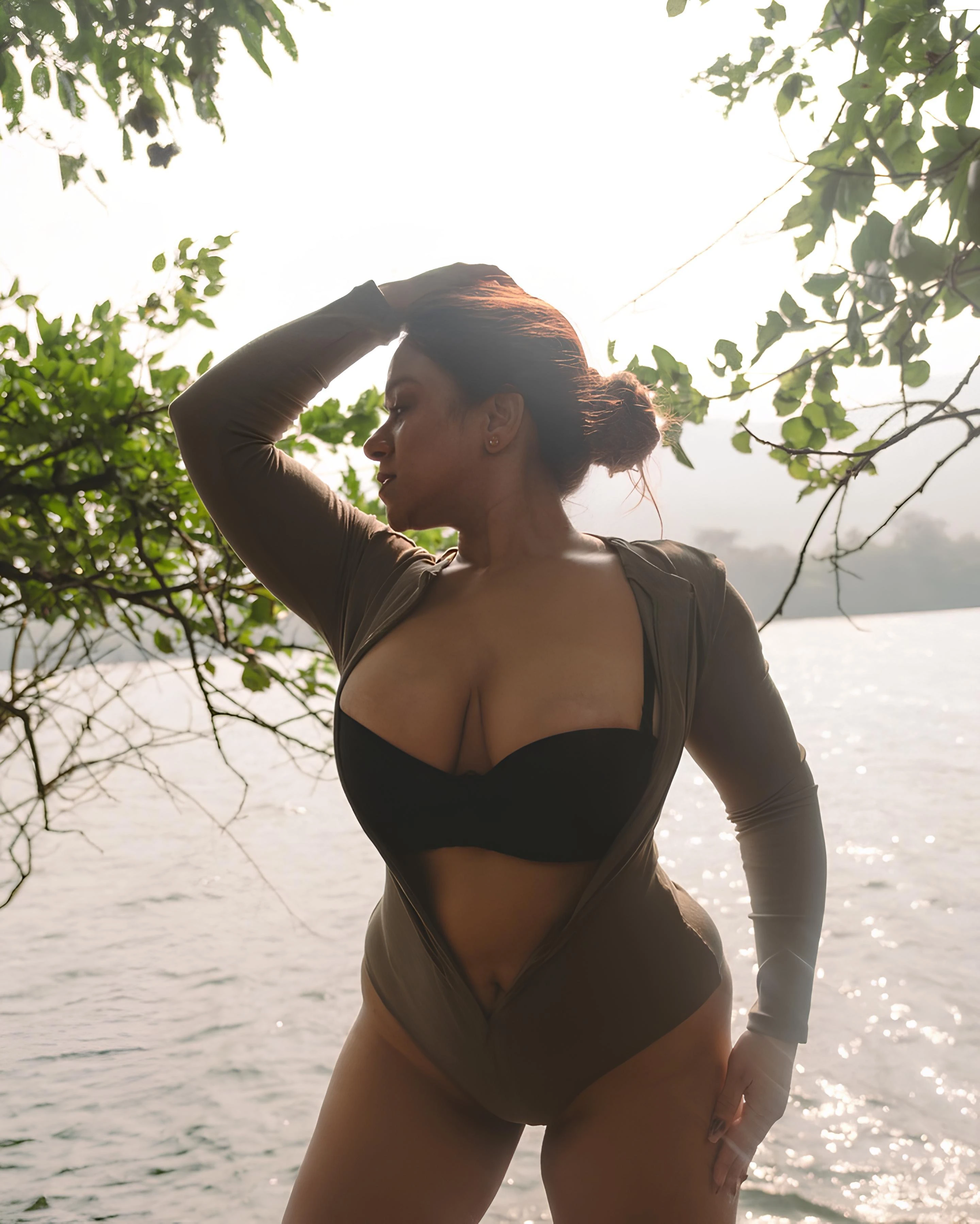 Curvy Desi MILF with brown hair rocking a black bra and olive green bodysuit, chilling by a lake
