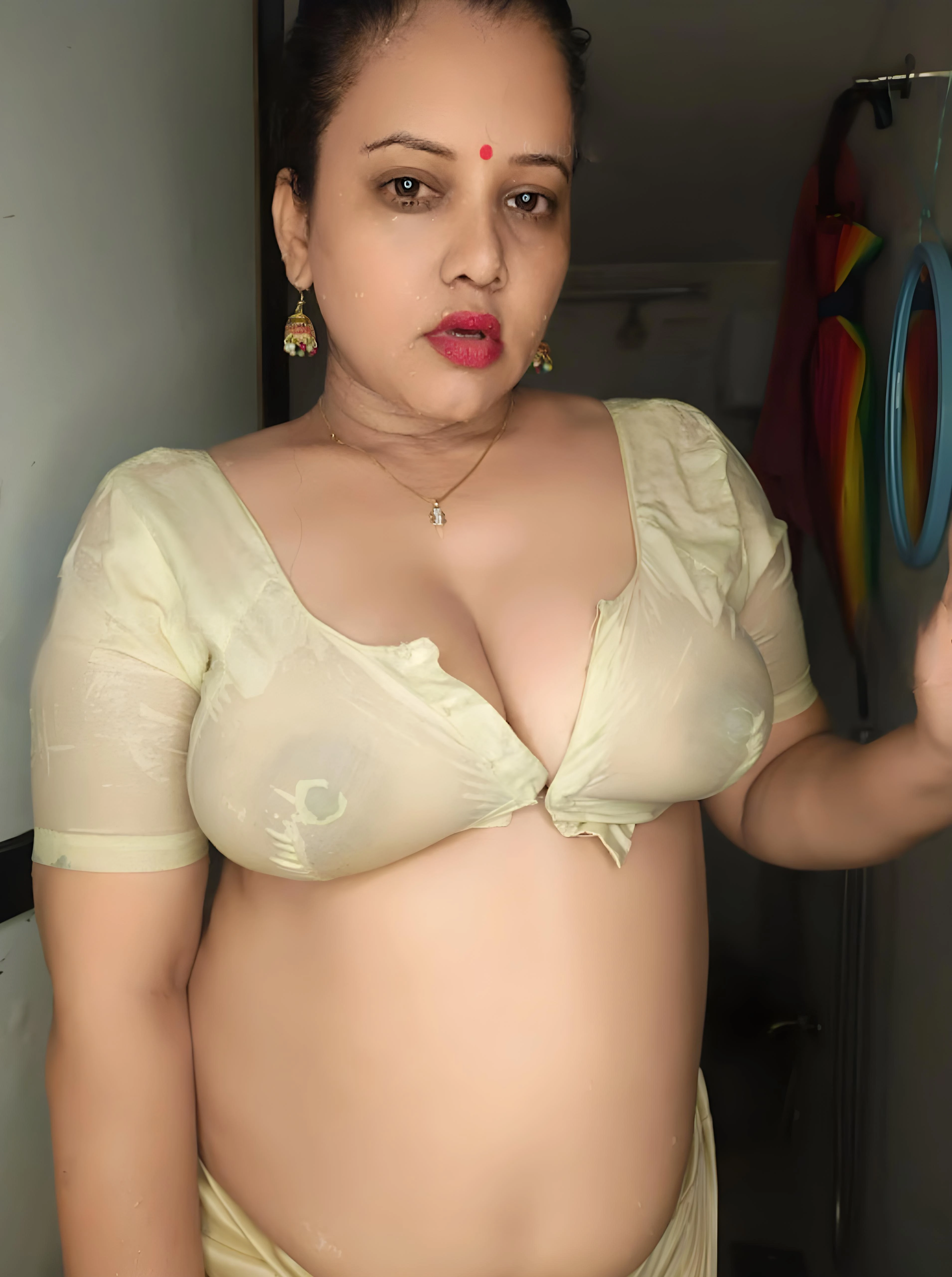 Sexy Desi MILF in a wet, transparent blouse, revealing her big boobs and nipples, stands confidently inside the bathroom