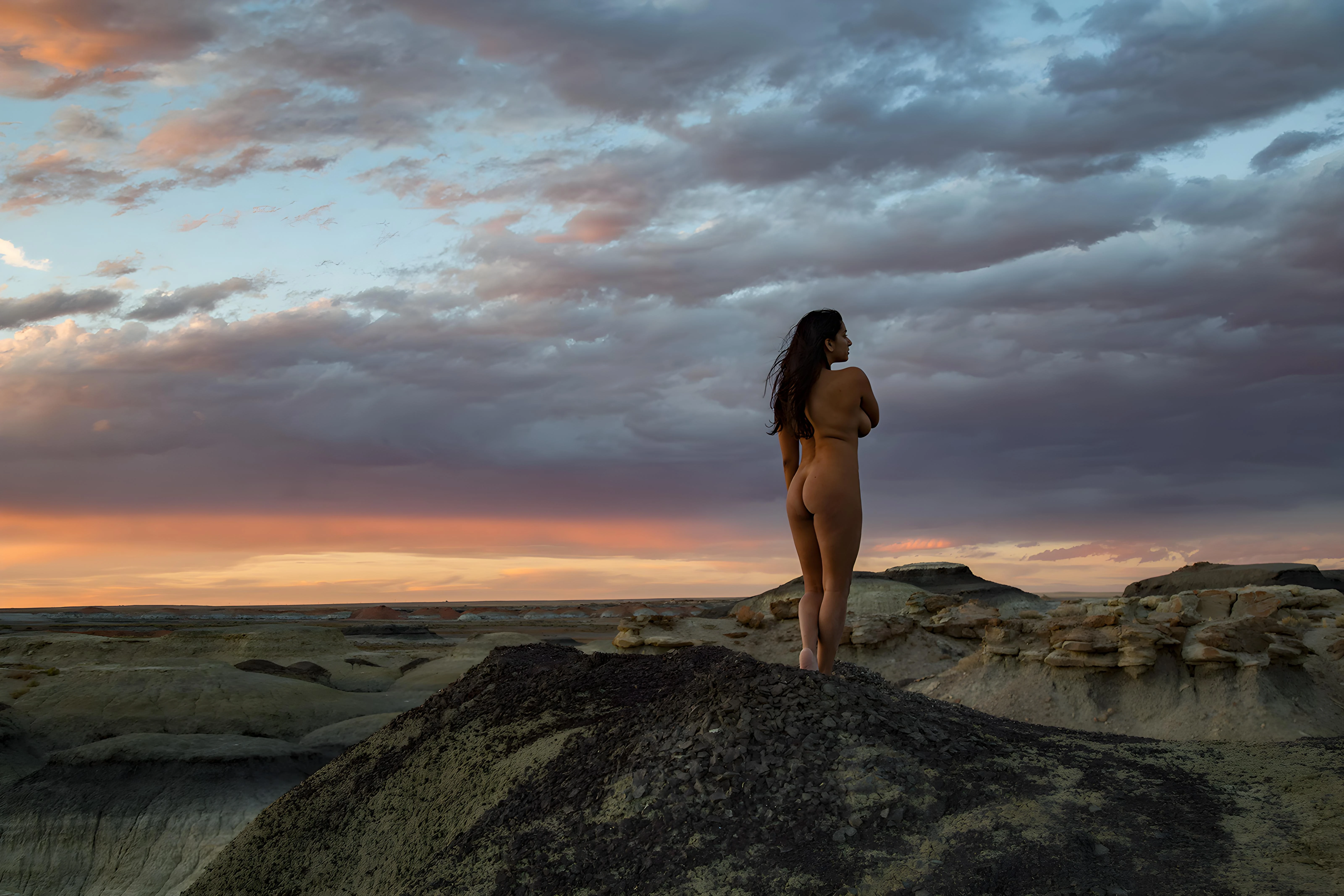 Sultry Desi vixen stands confidently on a rocky outcrop at sunset, showcasing her curvy physique and natural beauty against a dramatic sky