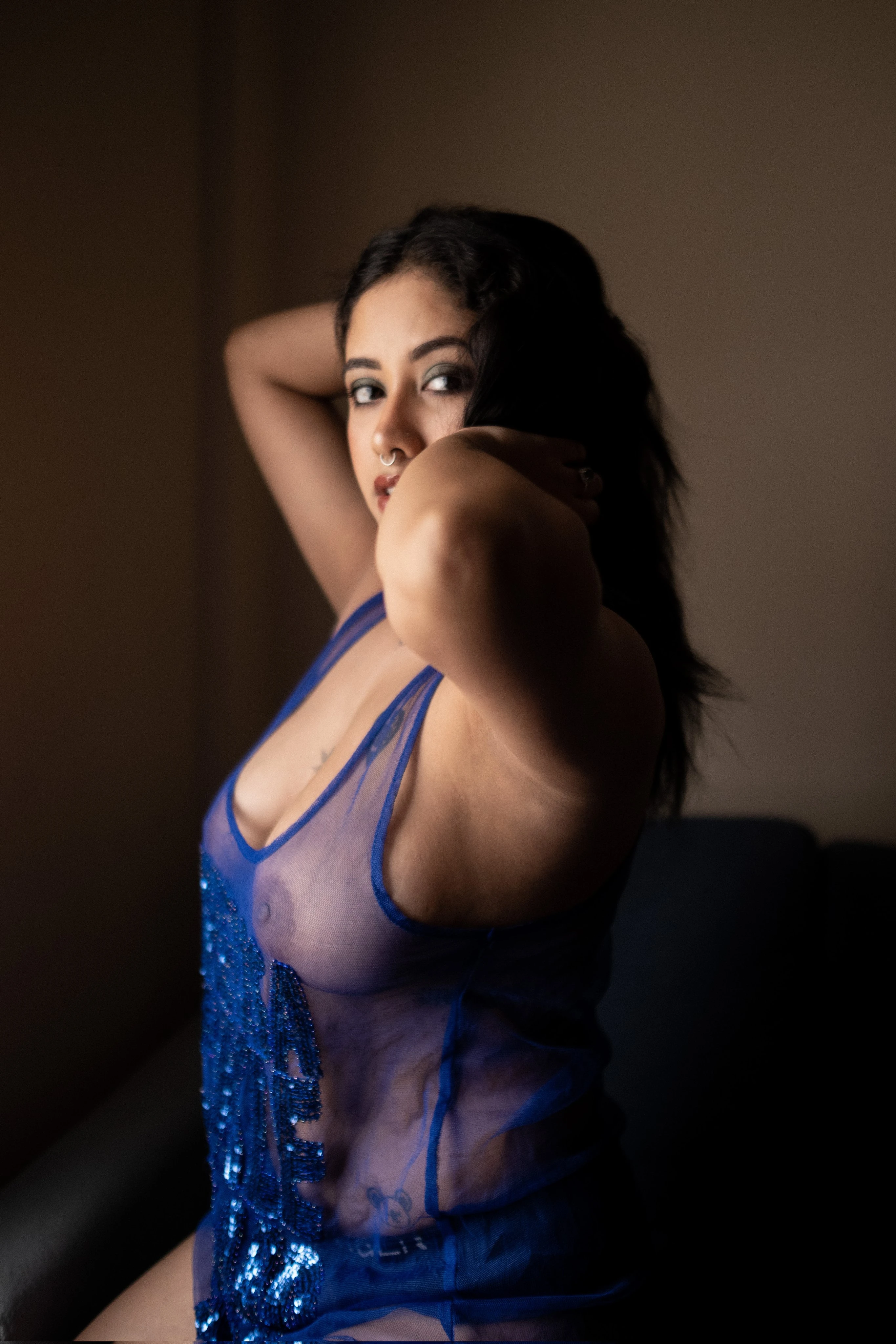 Desi model displays her large, round tits and dark nipples clearly through a sheer violet lingerie top, her gaze intense and direct