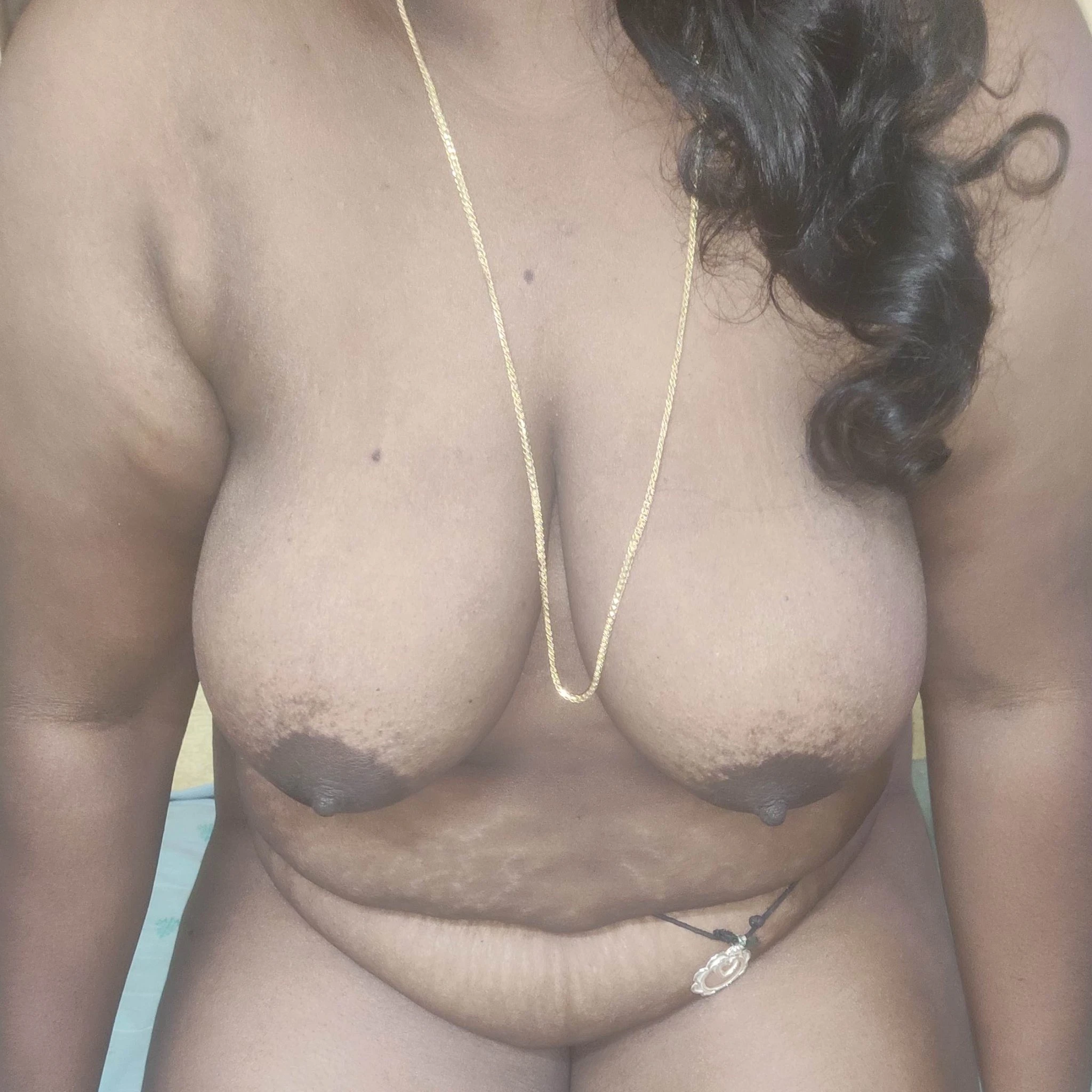 Nude Desi woman displaying full, hanging D-cup breasts with large, dark brown areolas, erect nipples, and a torso featuring visible stretch marks