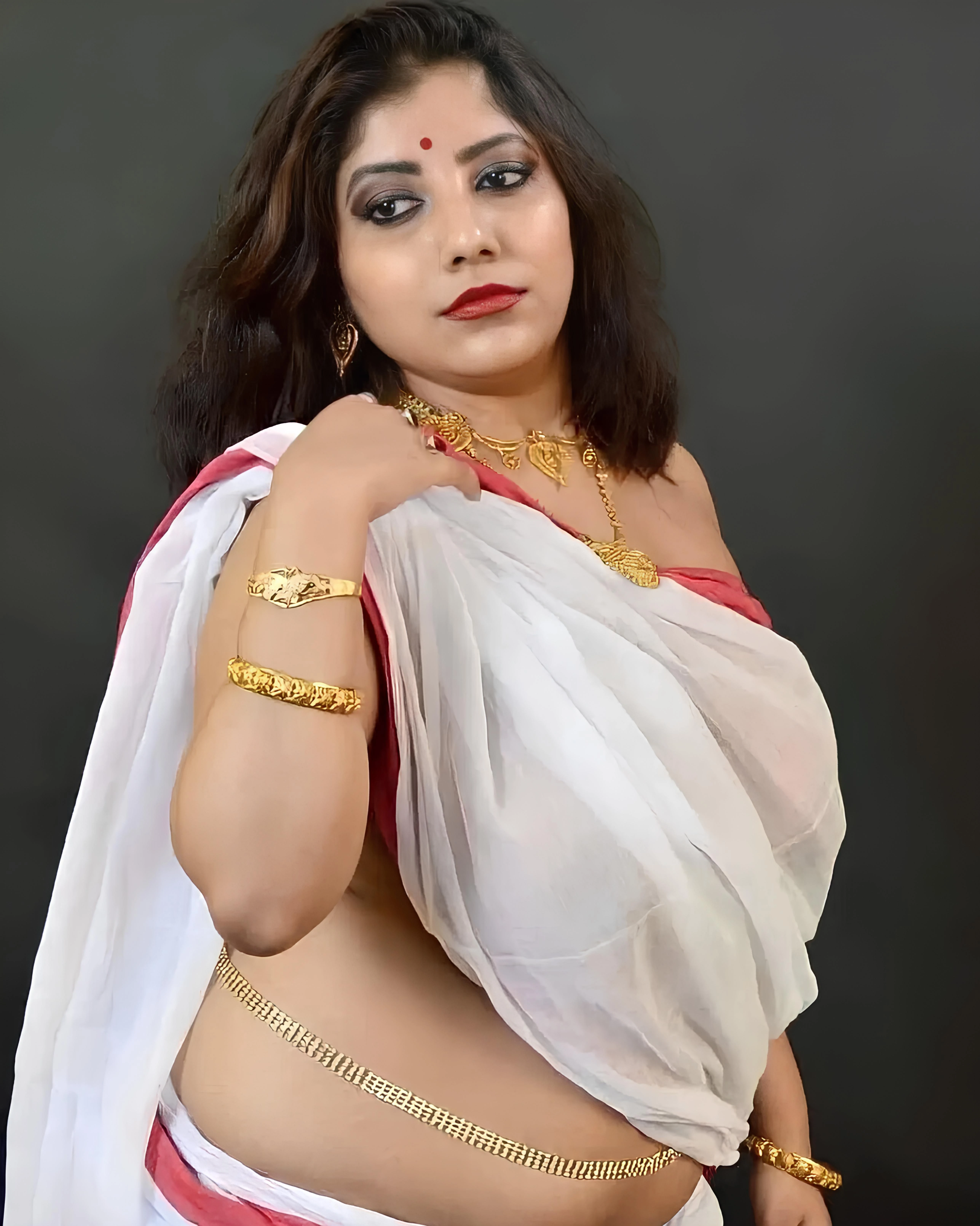 Desi MILF model with gold jewelry and red bindi displaying her large round breasts with visible nipples through thin braless white saree