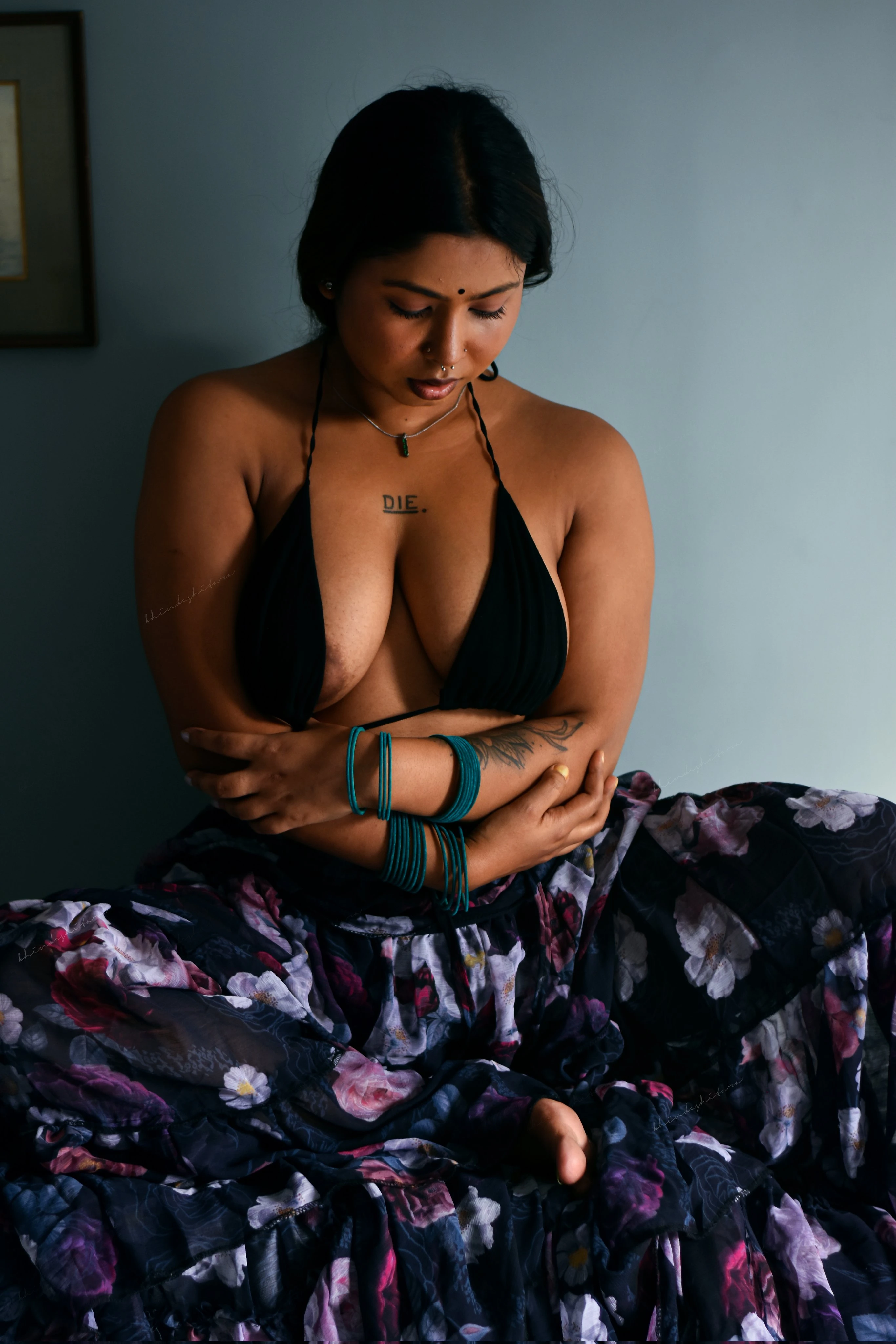 Desi model Bhindeshitara showing her full nipples peeking out of a black halter top seated amidst a cascade of vibrant floral skirt