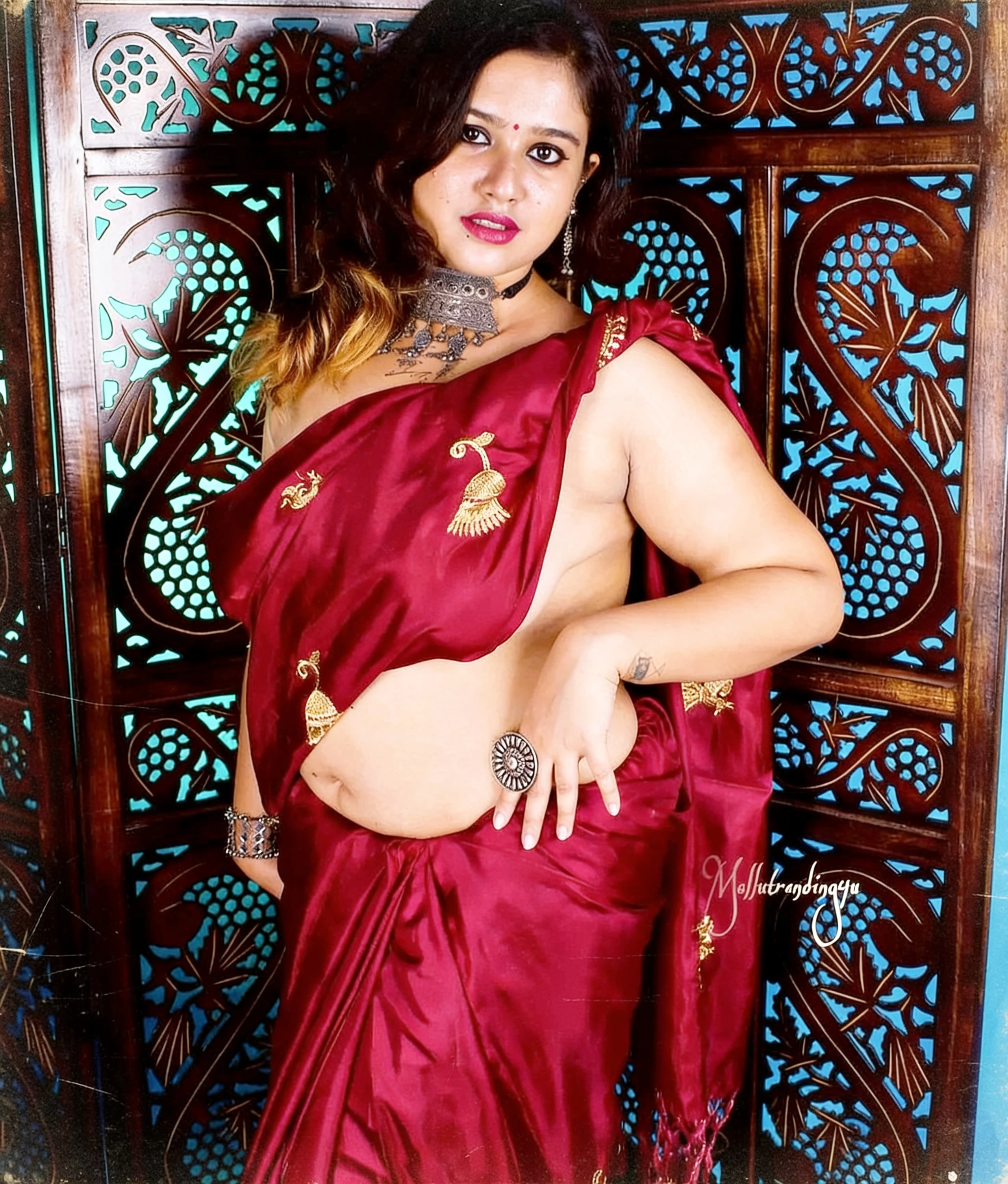 Desi woman with exposed left breast and gold jewelry poses confidently in a red braless saree