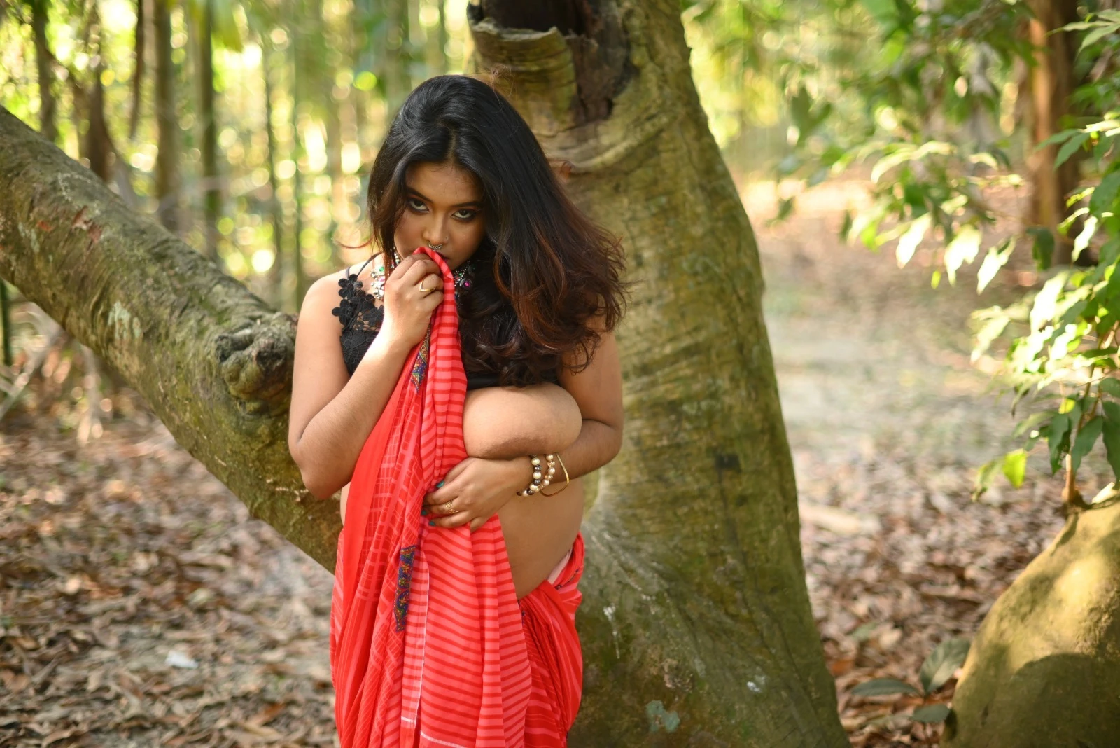 Ishani Das with big heavy tits revealing one large breast in a striped saree stands exhibitionist in a dense forest